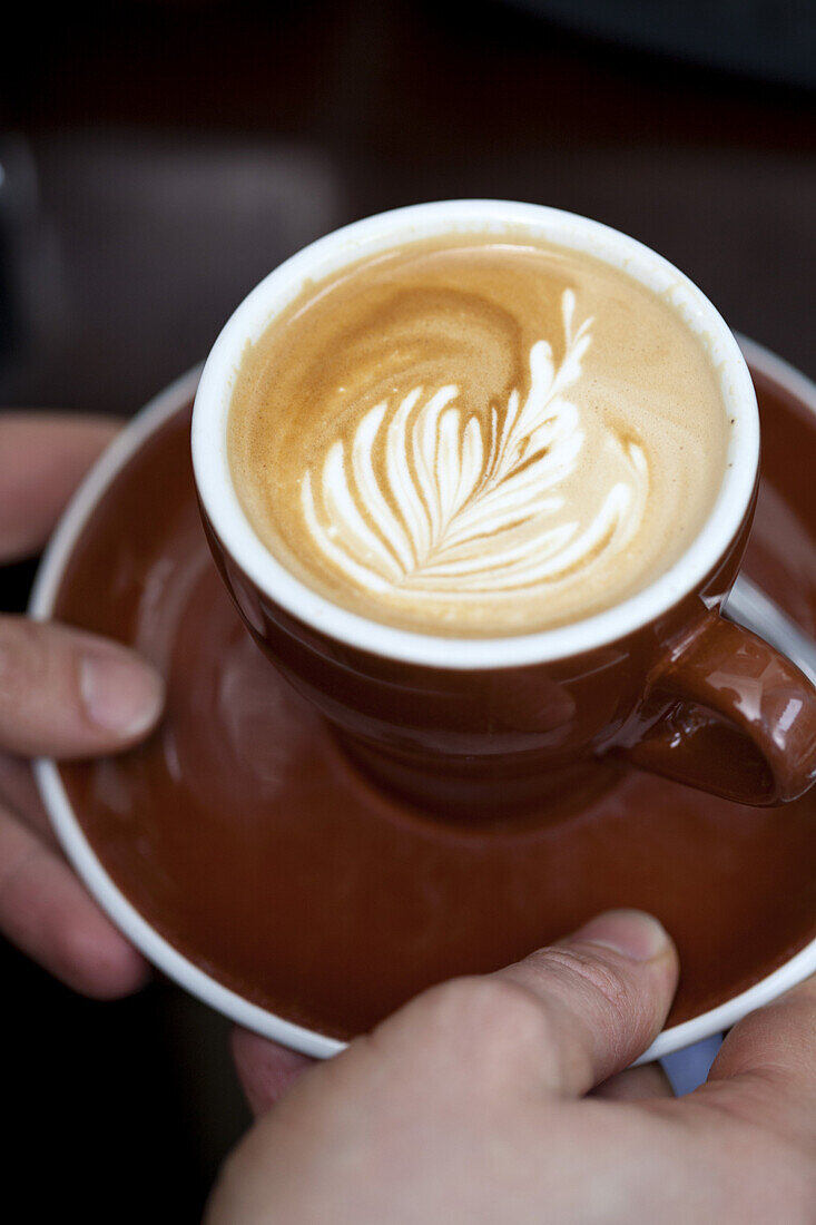 A barista serving a cappuccino with a floral pattern in the milk froth