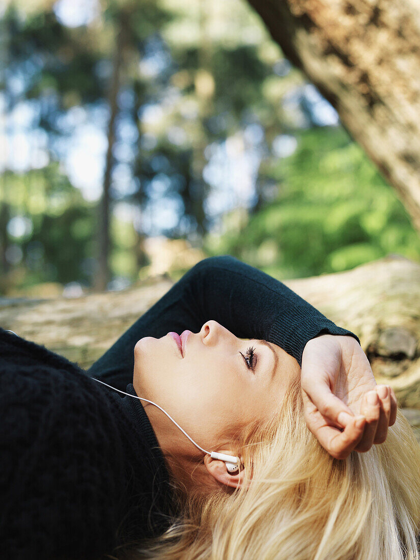 A woman lying outdoors wearing earphones, close-up, head and shoulders