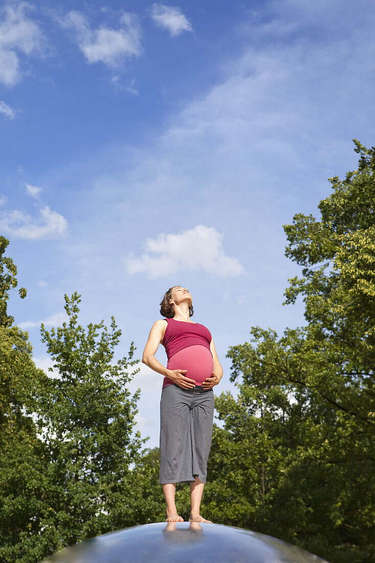 A pregnant woman standing in nature basking in the sun
