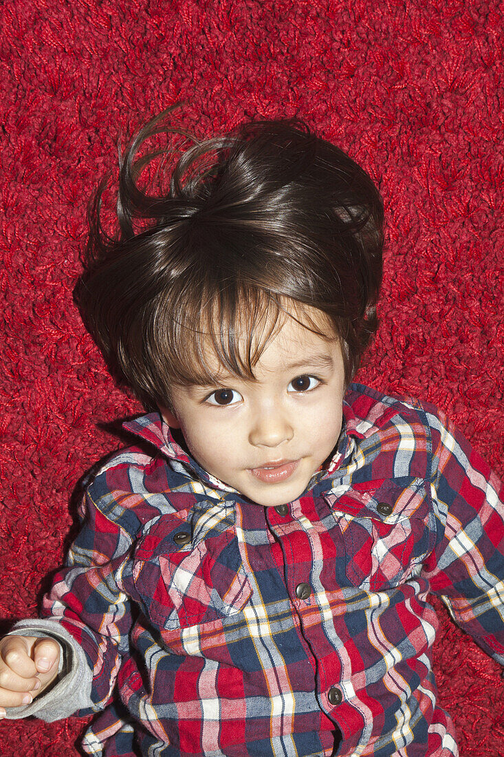 A young boy lying on a red carpet