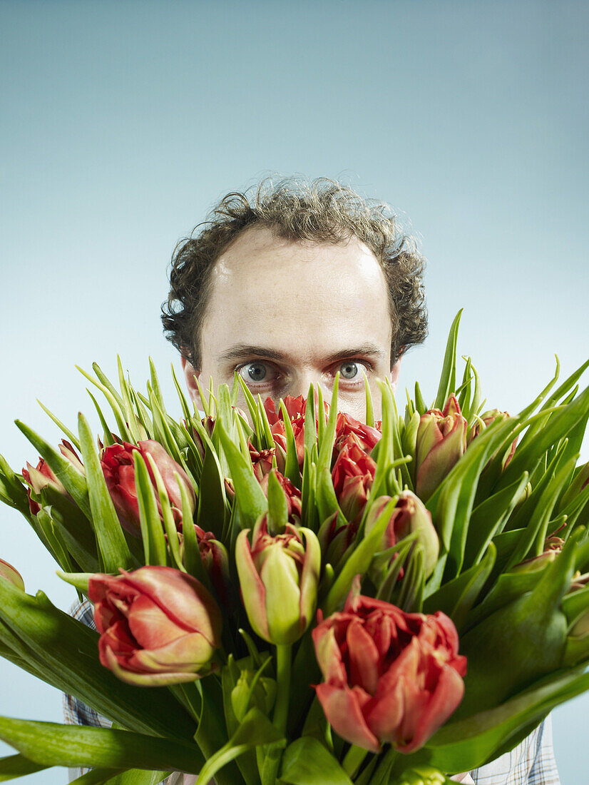 A man nervously hiding behind a bouquet of tulips