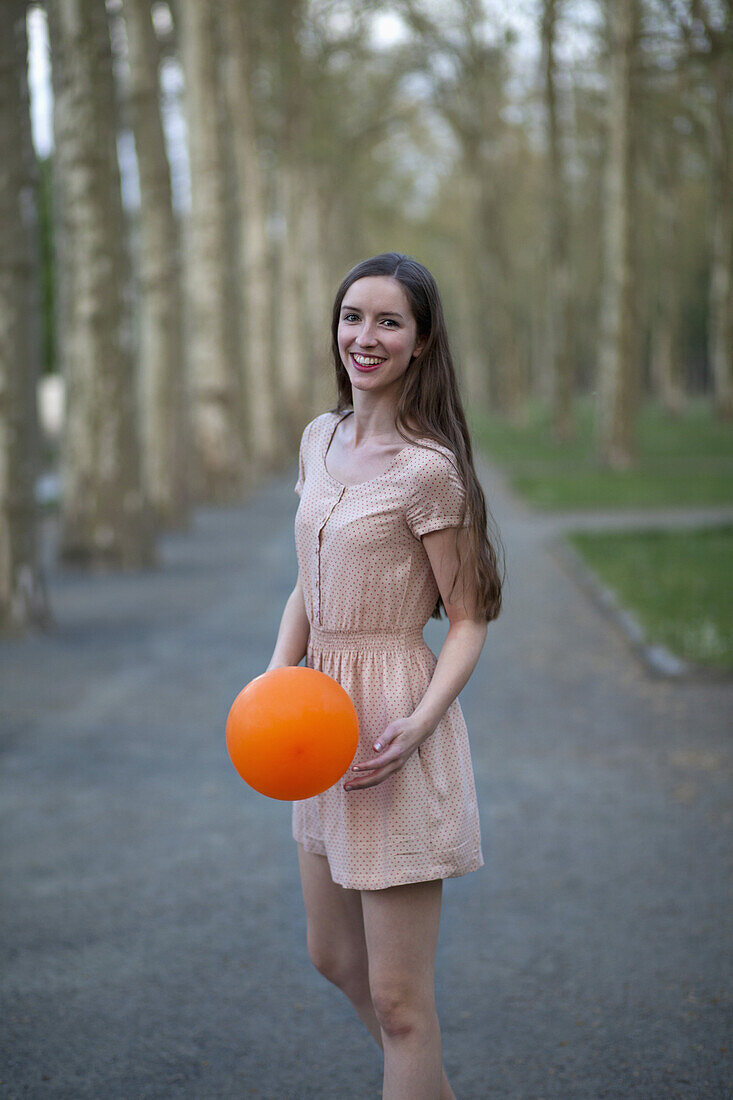 A young woman holding an orange ball, standing in a park