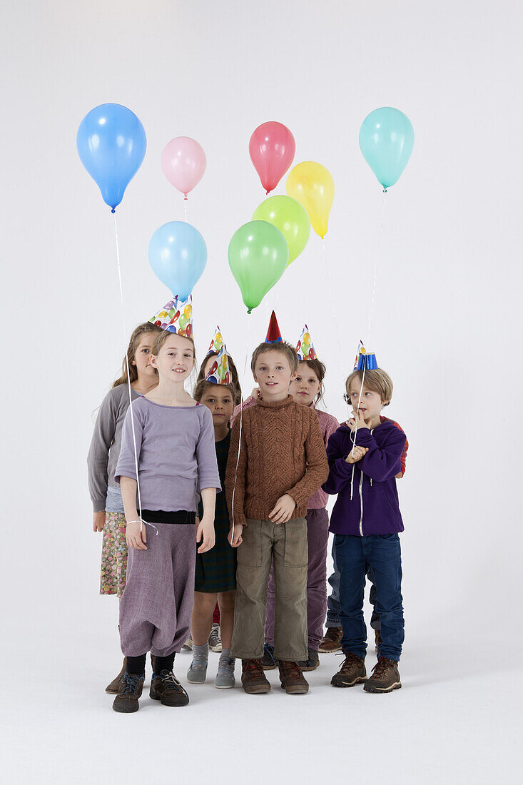 A group of kids wearing party hats and holding balloons
