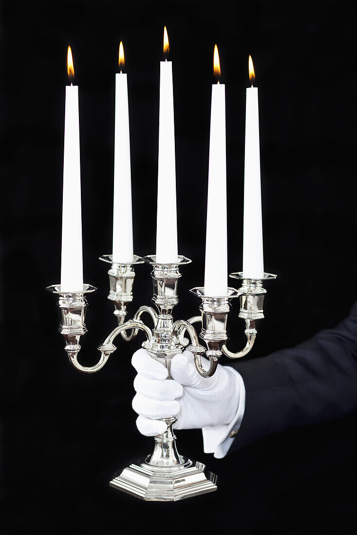 A butler holding a candelabra with lit candles, focus on hand
