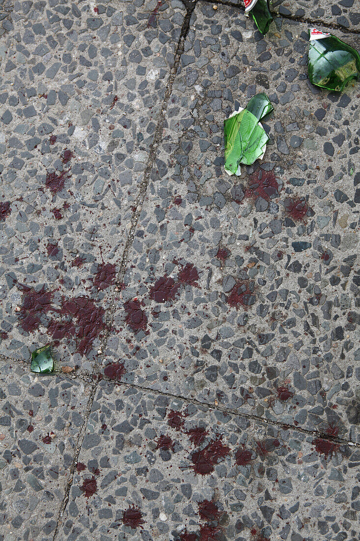 A broken beer bottle and splattered blood on a sidewalk