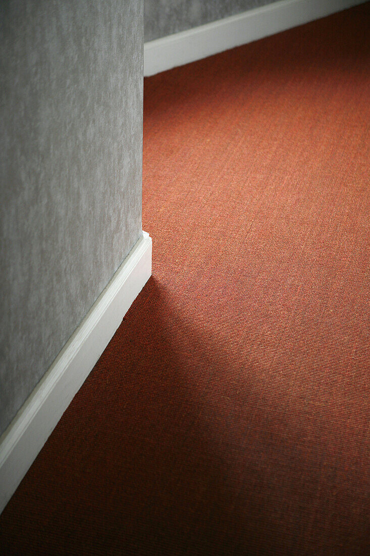 Contrasts of red carpet against white baseboard and gray wall