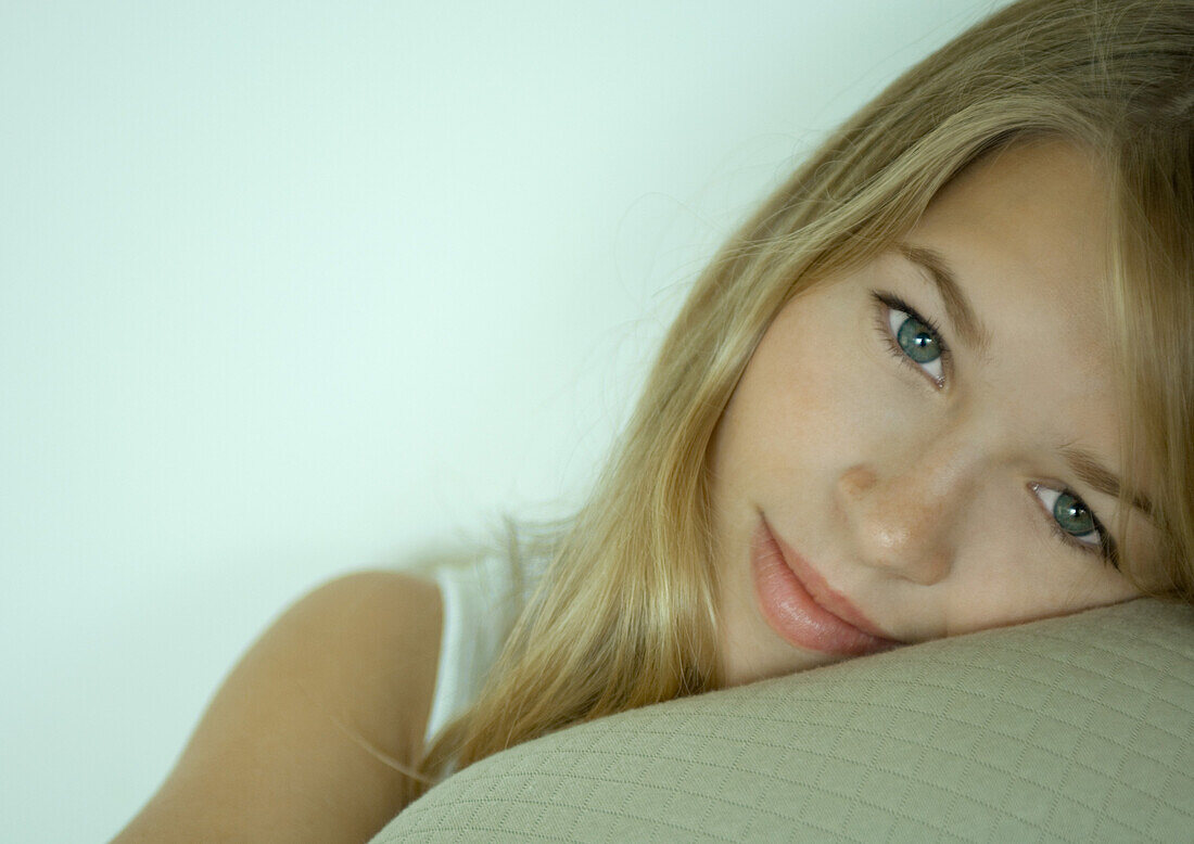 Young woman resting head on cushion, looking at camera