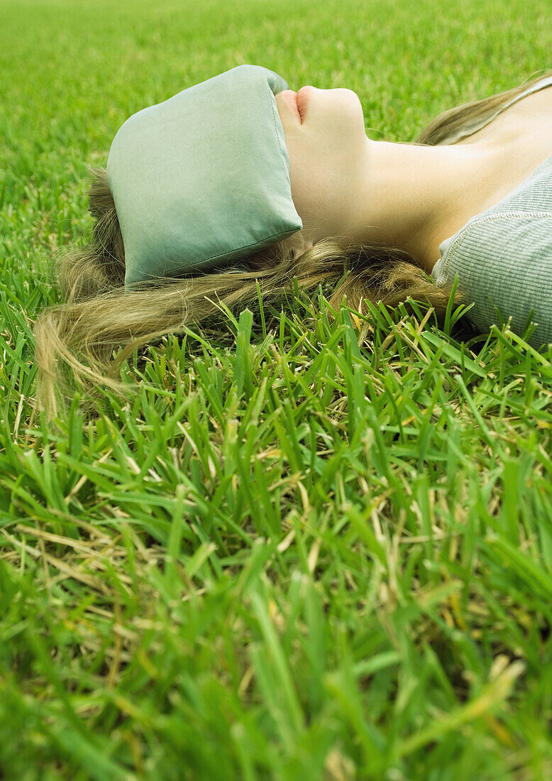 Young woman lying on grass with eye pillow covering eyes