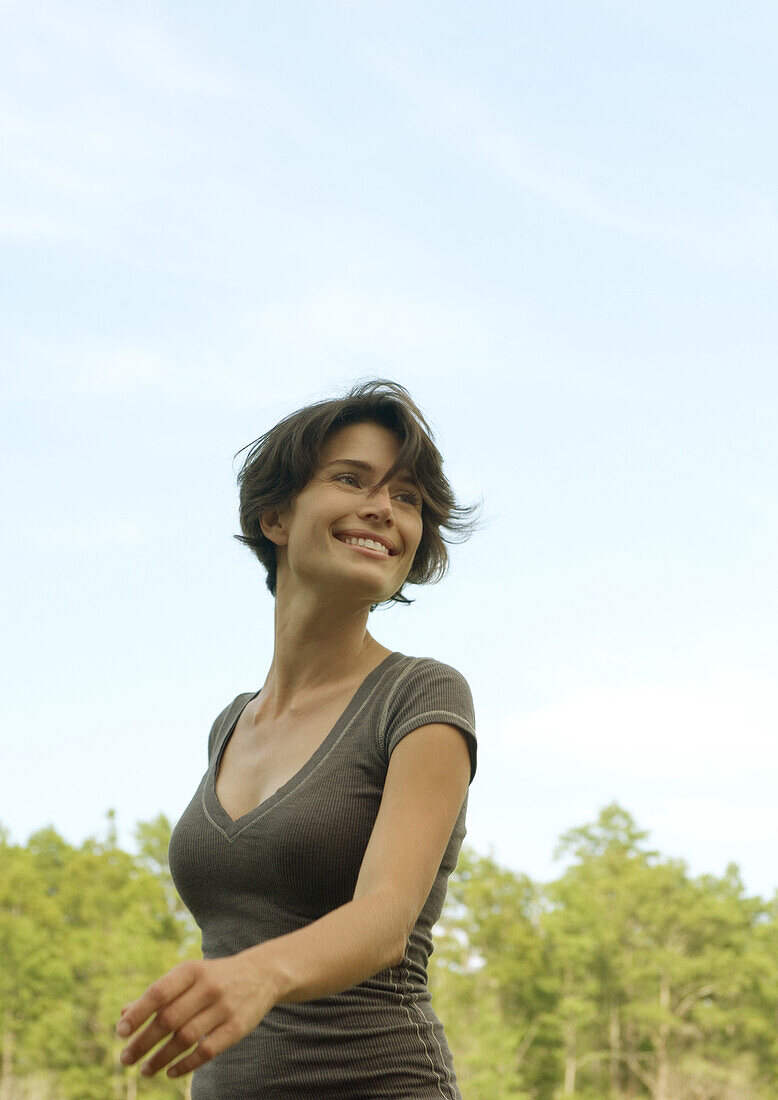 Woman walking outdoors, smiling, trees in background