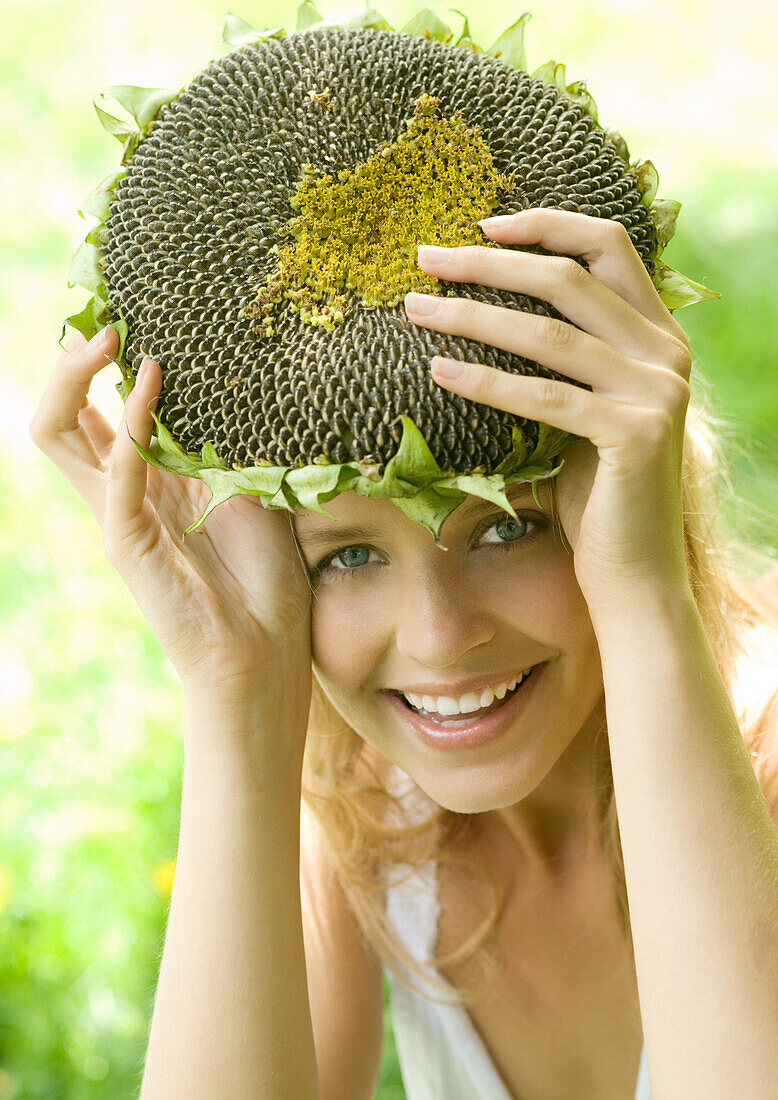 Young woman holding up dried sunflower over head