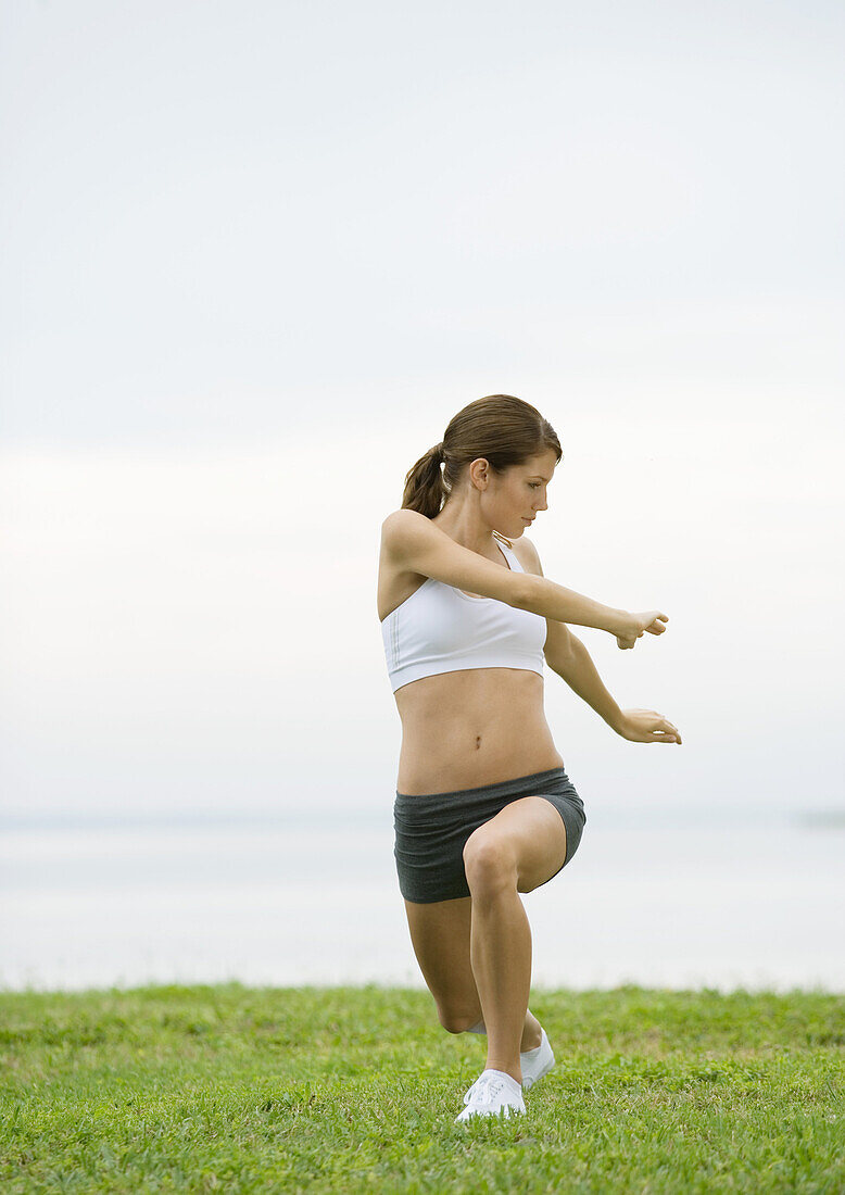 Young woman doing stretching exercises by lakeside