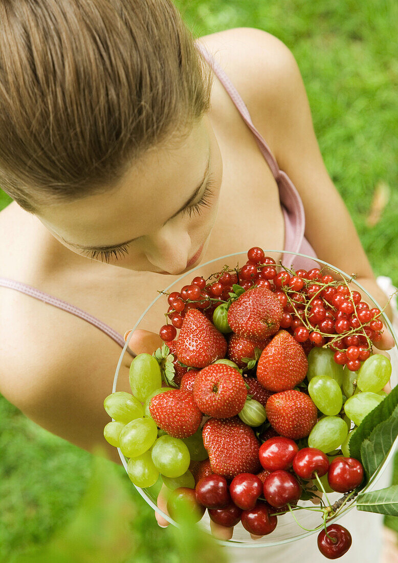 Young woman holding up bowl of fruit