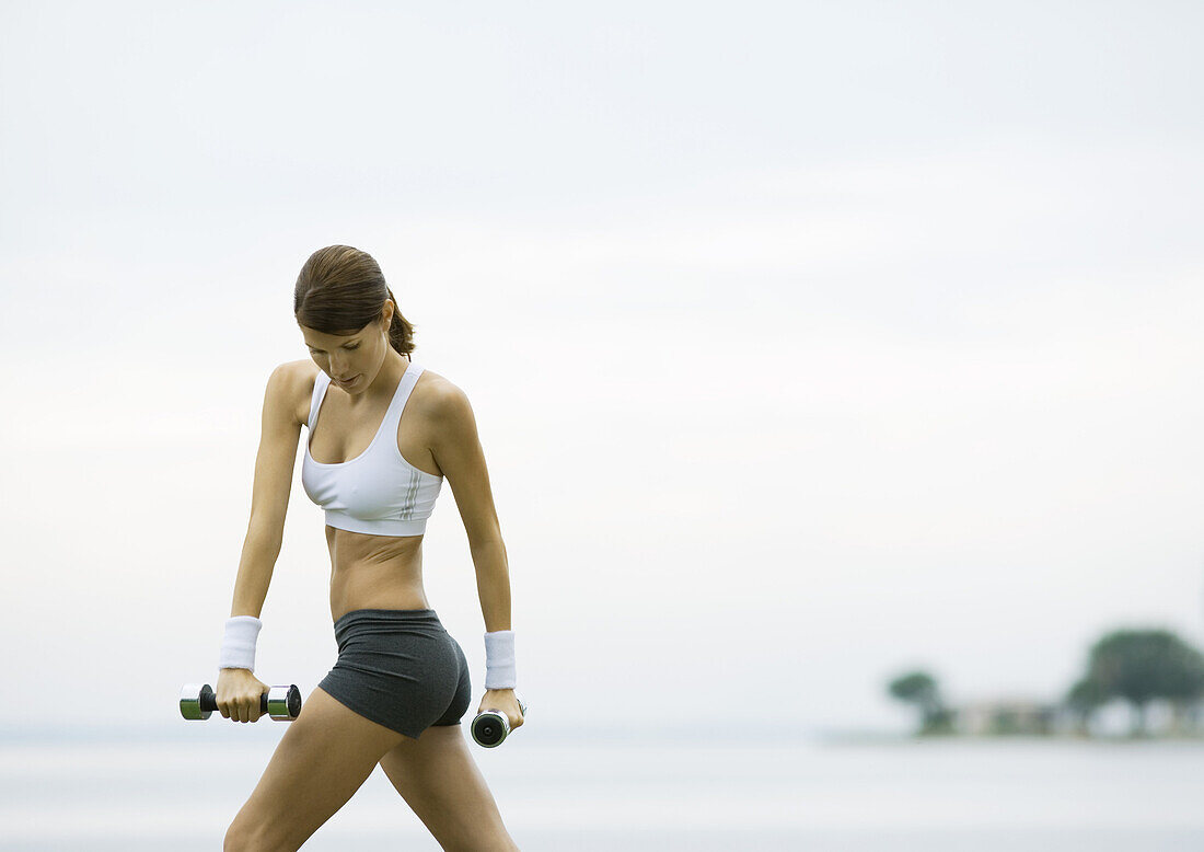 Junge Frau trainiert mit Gewichten am Seeufer