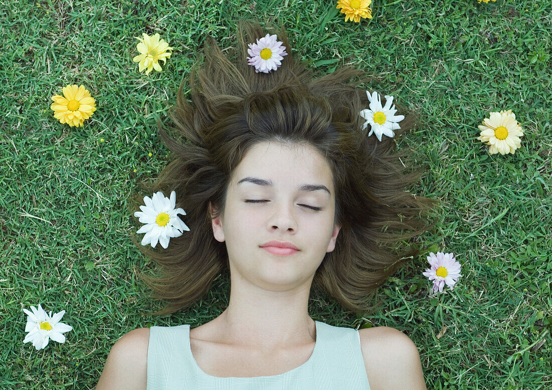 Woman lying on grass with flowers scattered around head, eyes closed