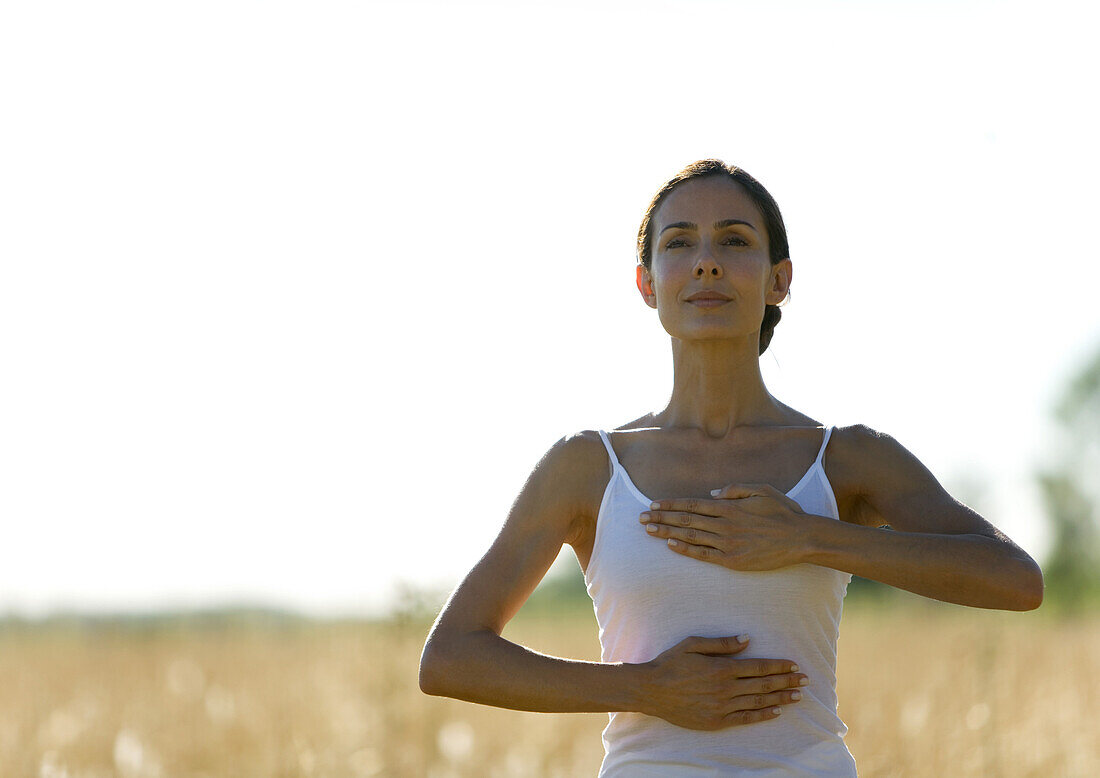 Woman in field, with hands on chest and stomach