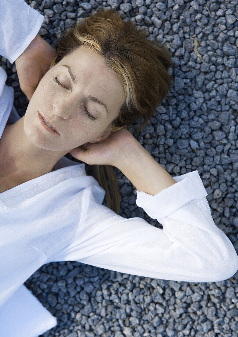 Woman lying on gravel with hands behind head, eyes closed