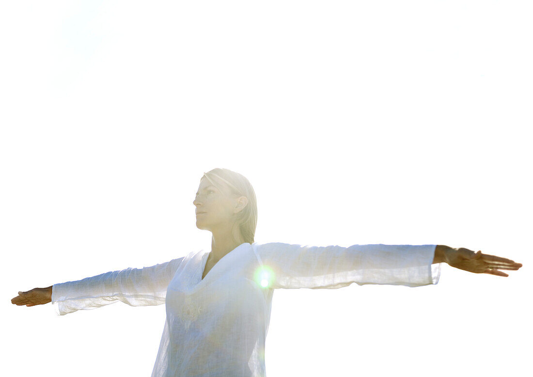 Woman standing with arms out, low angle view, backlit