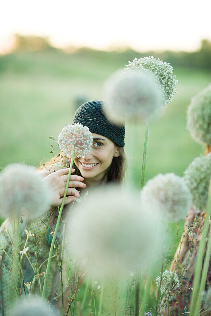 Young woman hiding behind allium flower, looking at camera