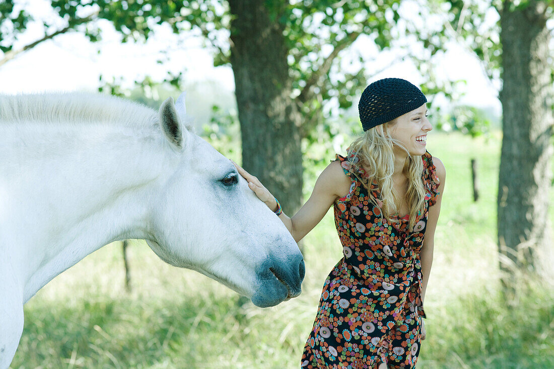 Young woman touching horse and laughing