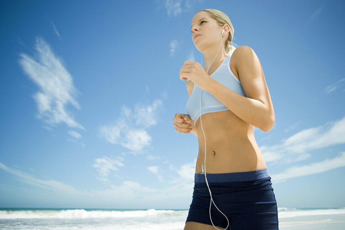 Young woman jogging on beach, listening to MP3 player, low angle view