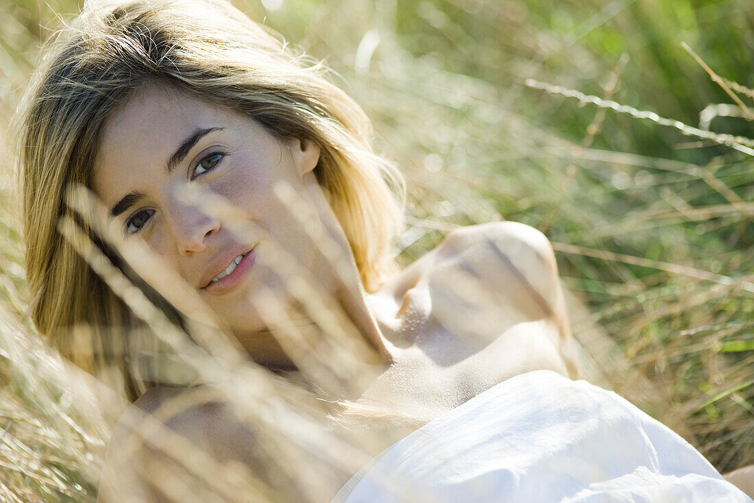 Young woman leaning back in tall grass, smiling at camera