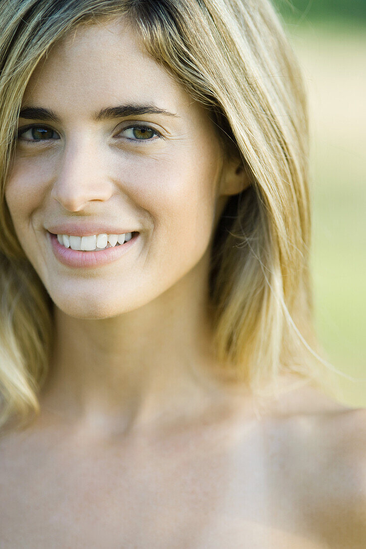 Young woman with bare shoulders smiling at camera, cropped portrait