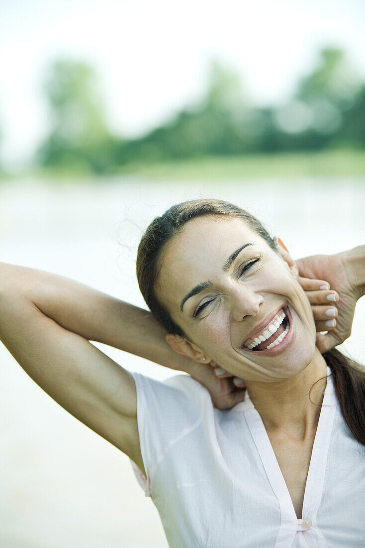 Woman outdoors, hands behind head, laughing, head and shoulders