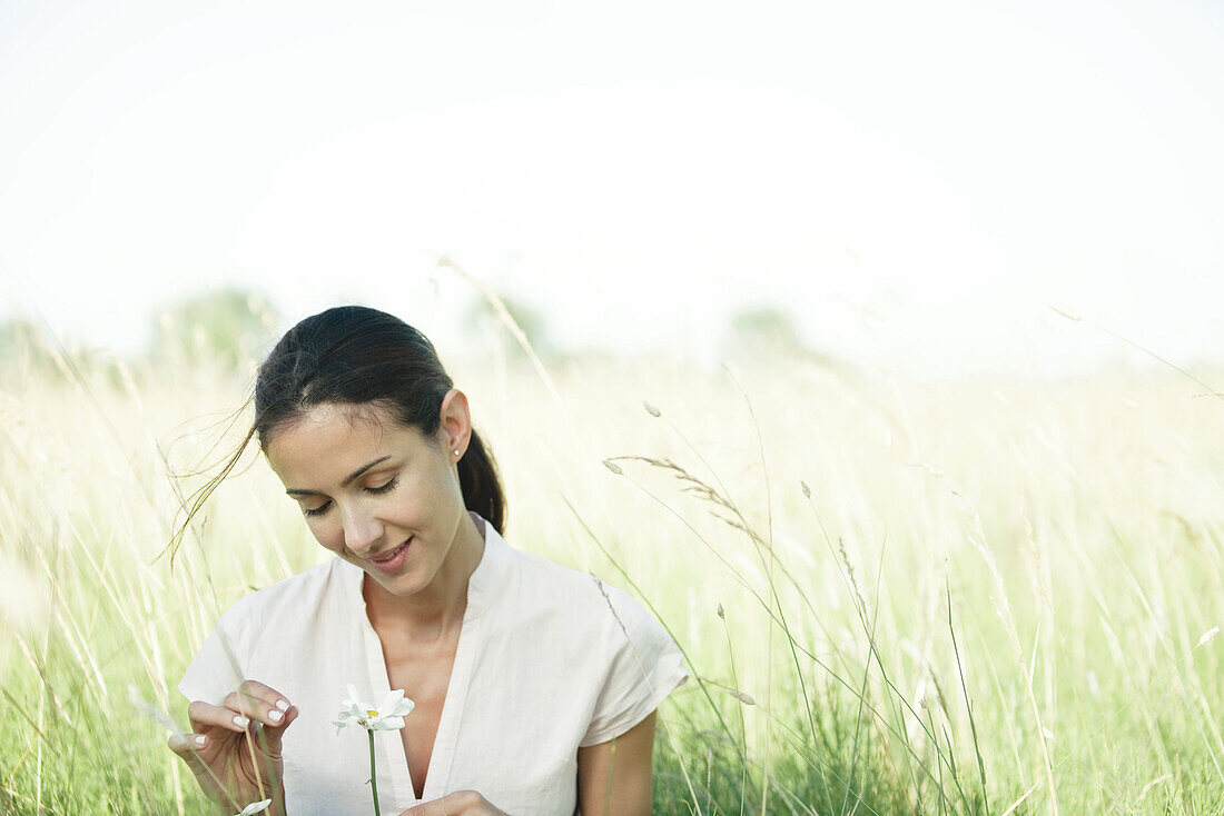 Woman in field, looking at flower, head and shoulders