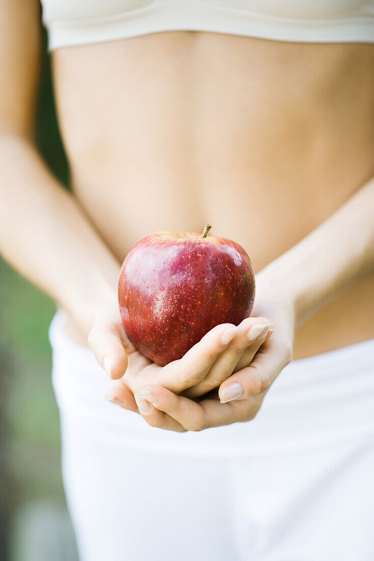 Woman holding apple in front of bare abdomen, close-up of mid section
