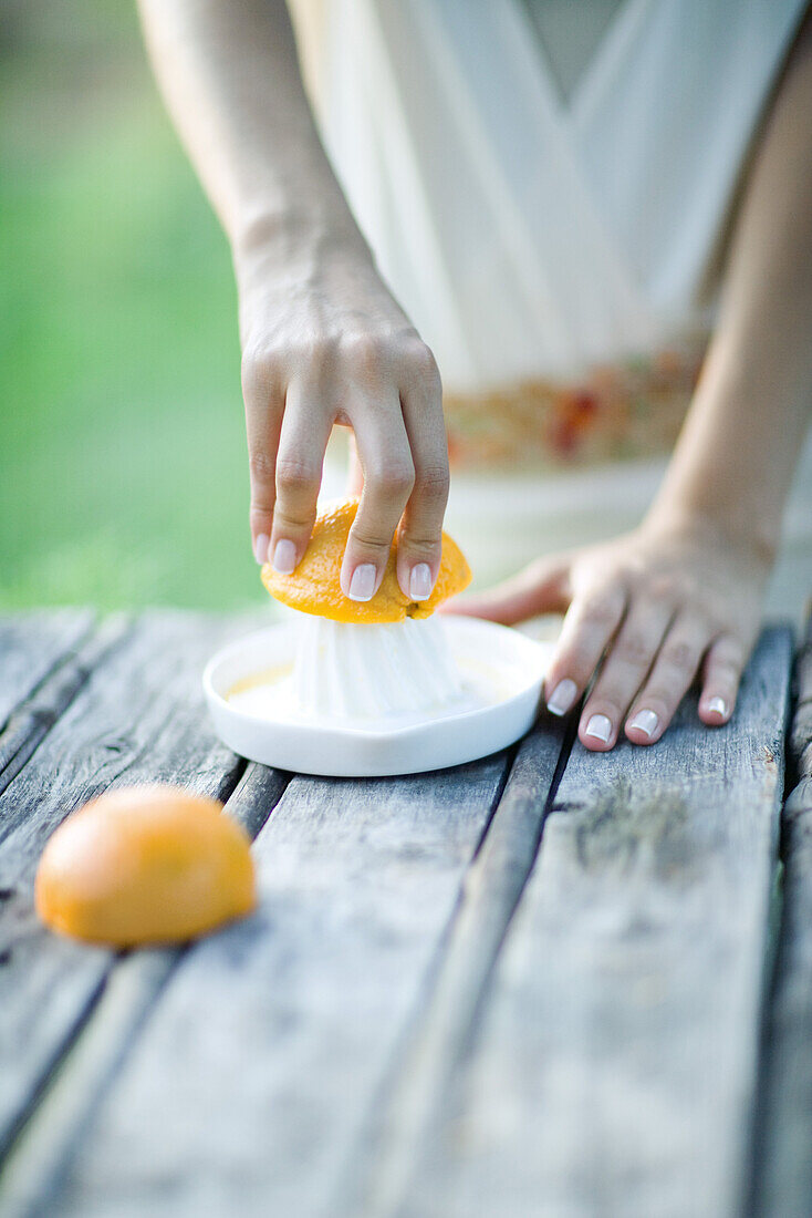 Woman pressing orange with citrus press, close-up, cropped view of hands