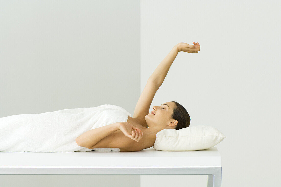 Woman lying on massage table, eyes closed, one arm raised
