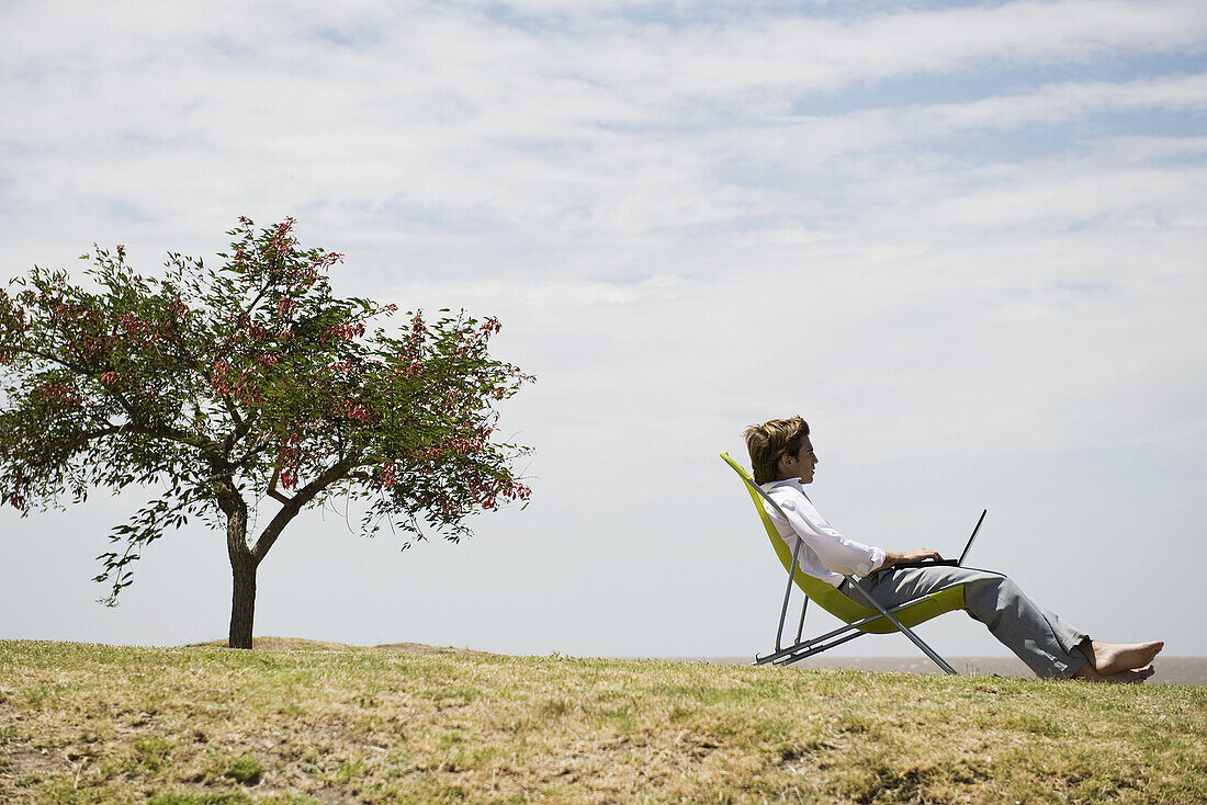 Man relaxing in lounge chair outdoors, using laptop computer