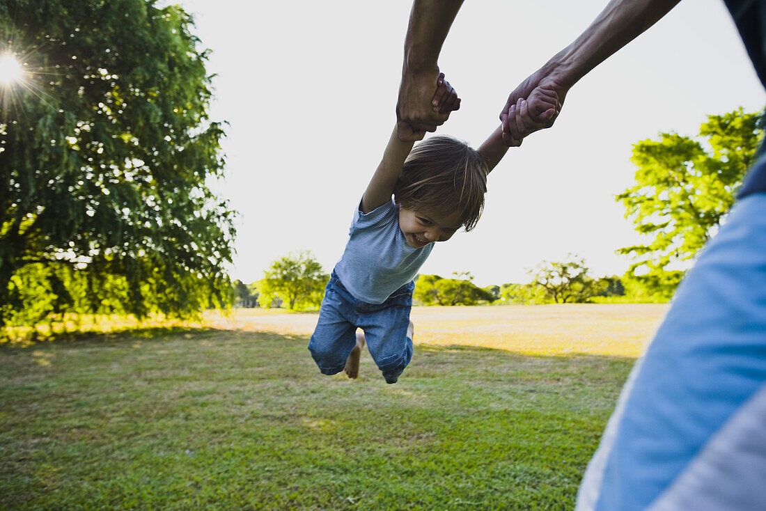 Parent spinning little boy in park