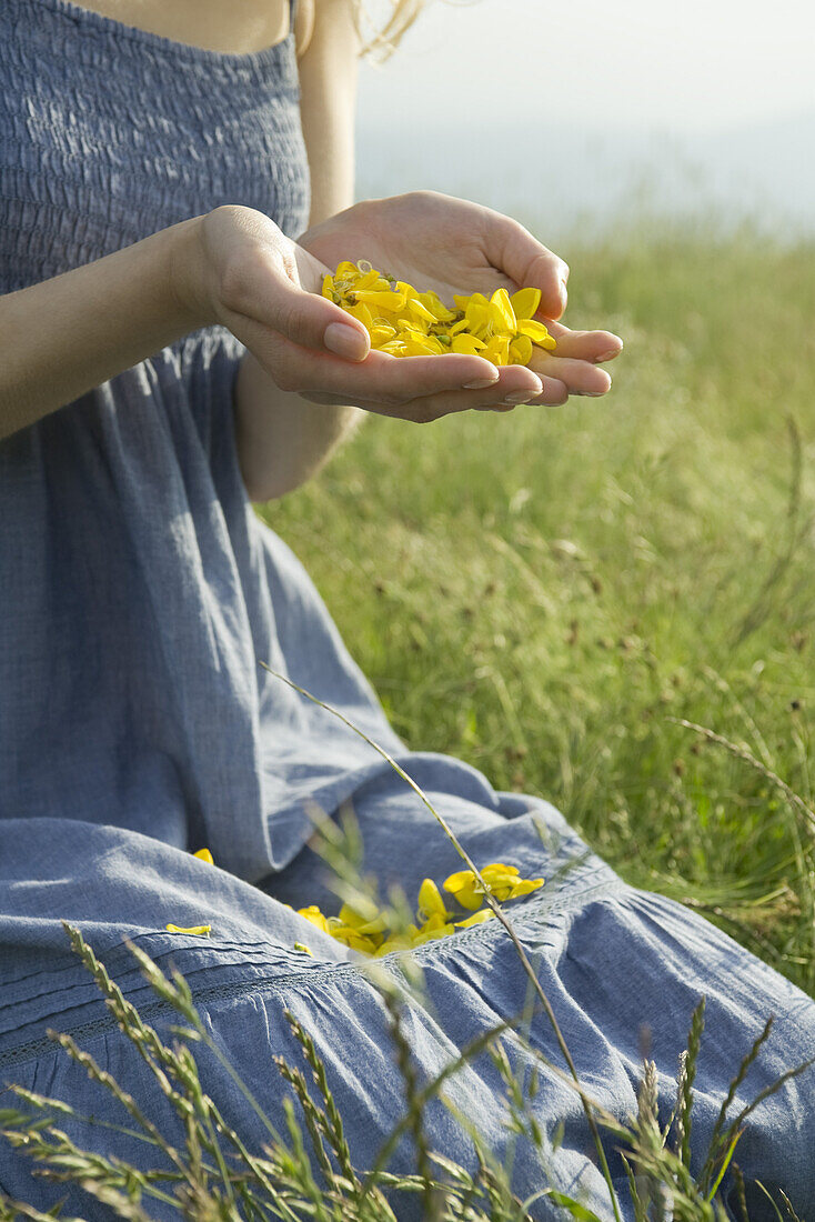 Junge Frau kniet auf einer Wiese und hält Blumenblätter in den Händen, Ausschnitt