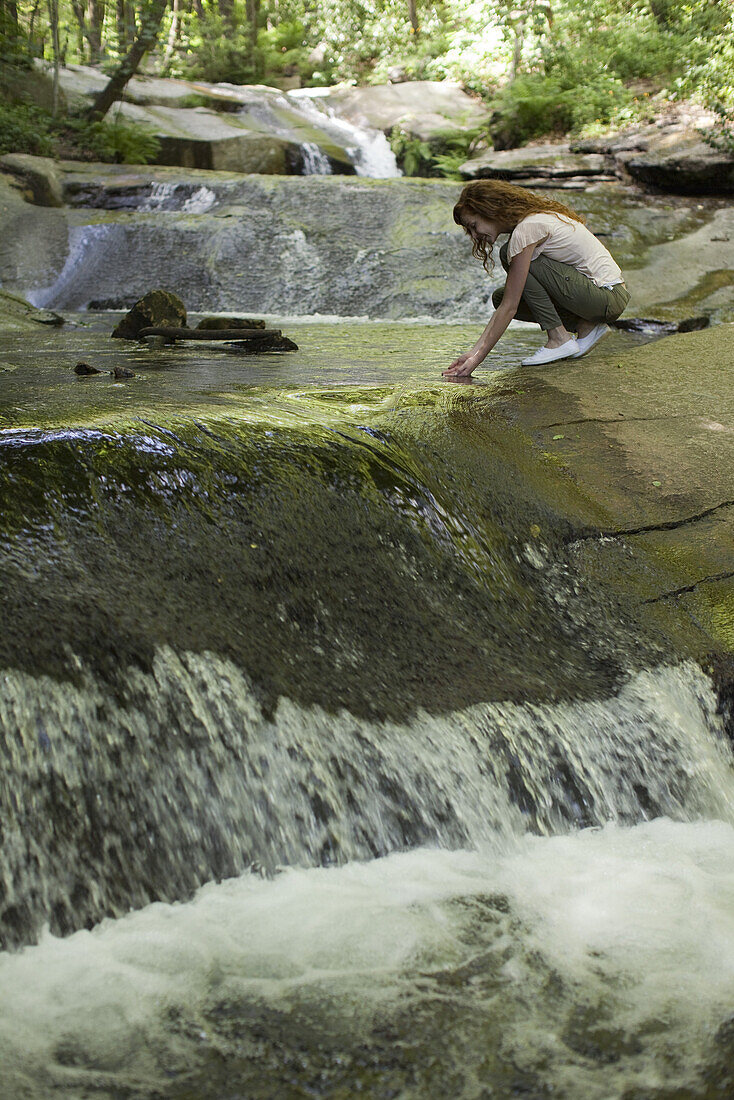 Woman crouching beside cascading stream, dipping hands in water