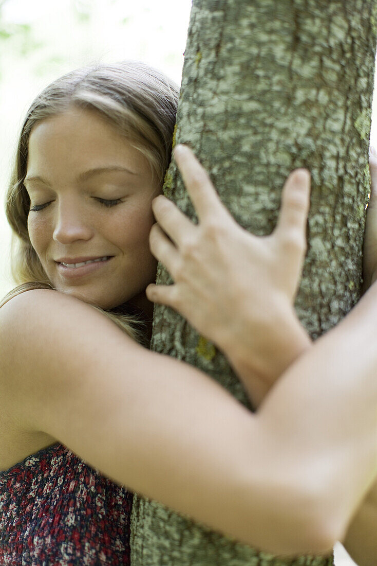 Young woman hugging tree with eyes closed