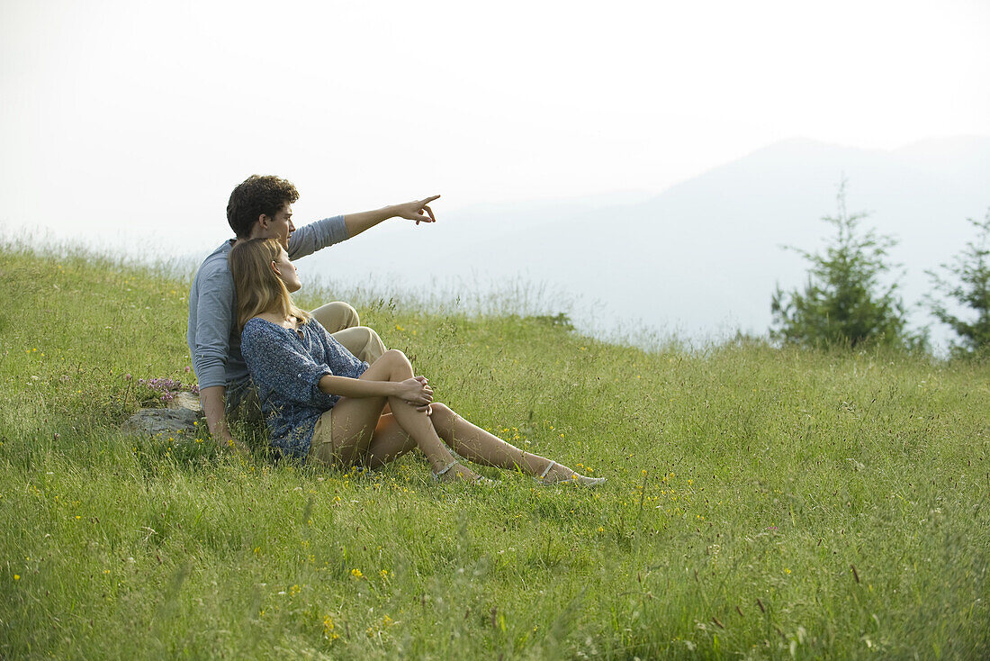 Couple sitting on meadow, man pointing toward distance