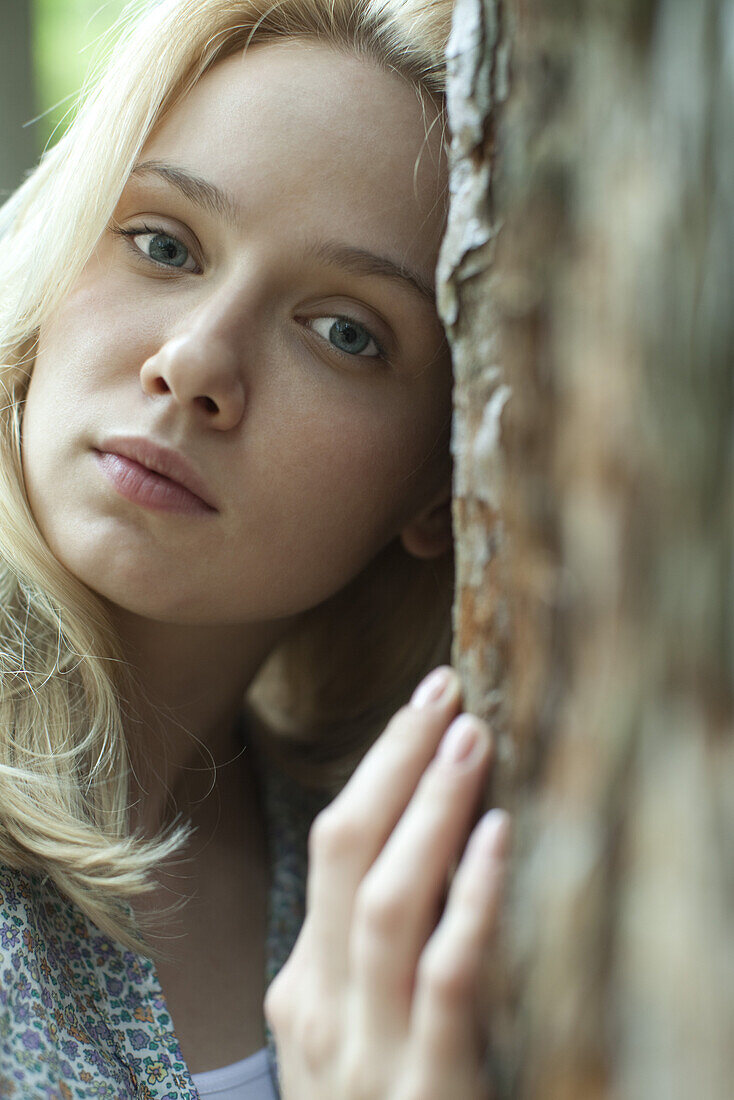 Young woman leaning against tree, portrait