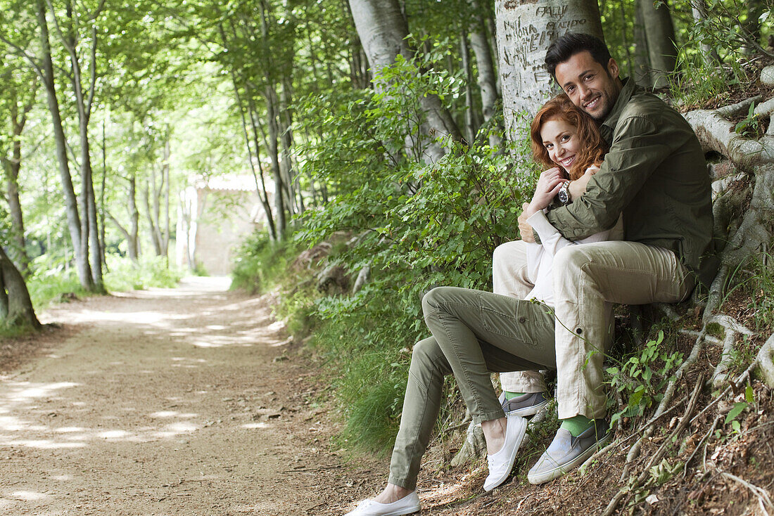 Couple sitting together beside wooded path, portrait
