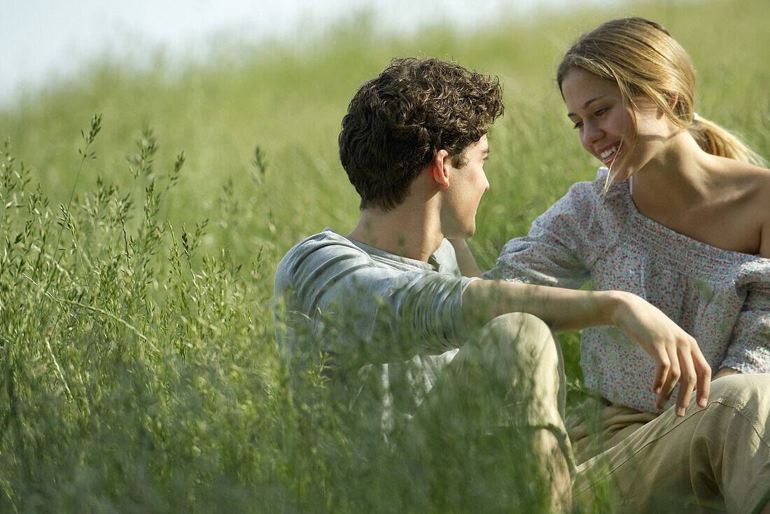 Couple sitting in grass, looking at each other affectionately