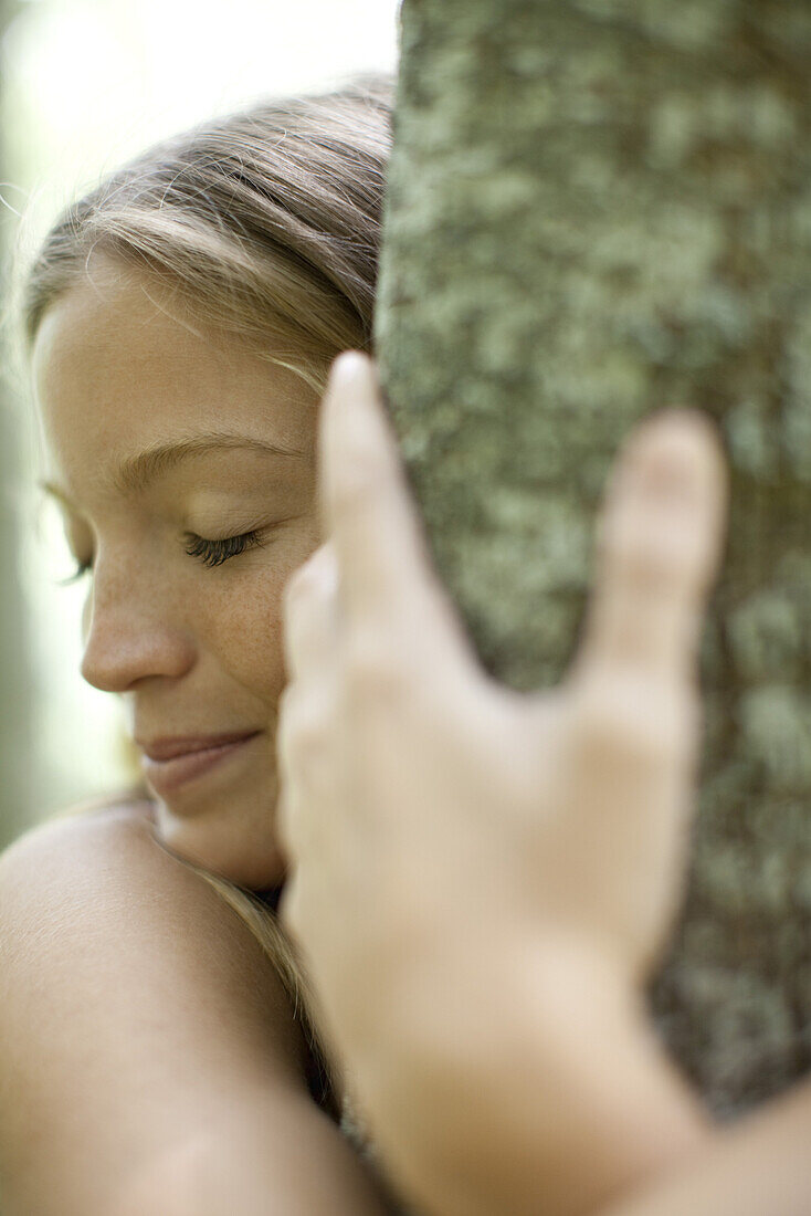 Young woman hugging tree with eyes closed, cropped