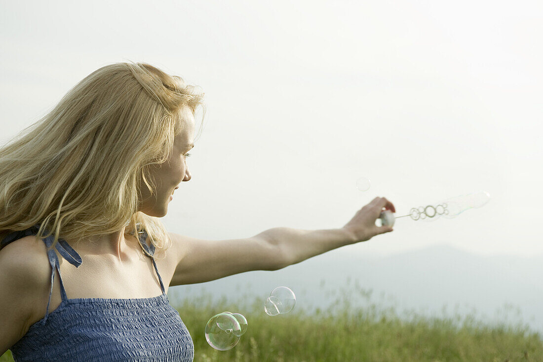 Young woman holding out bubble wand in wind