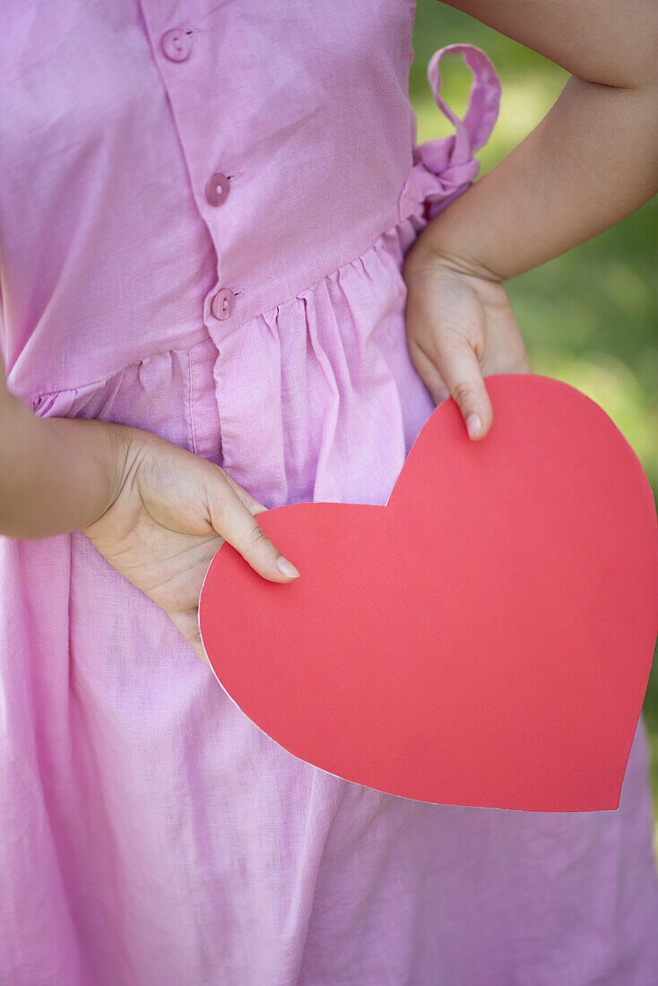 Girl holding paper heart behind back, cropped