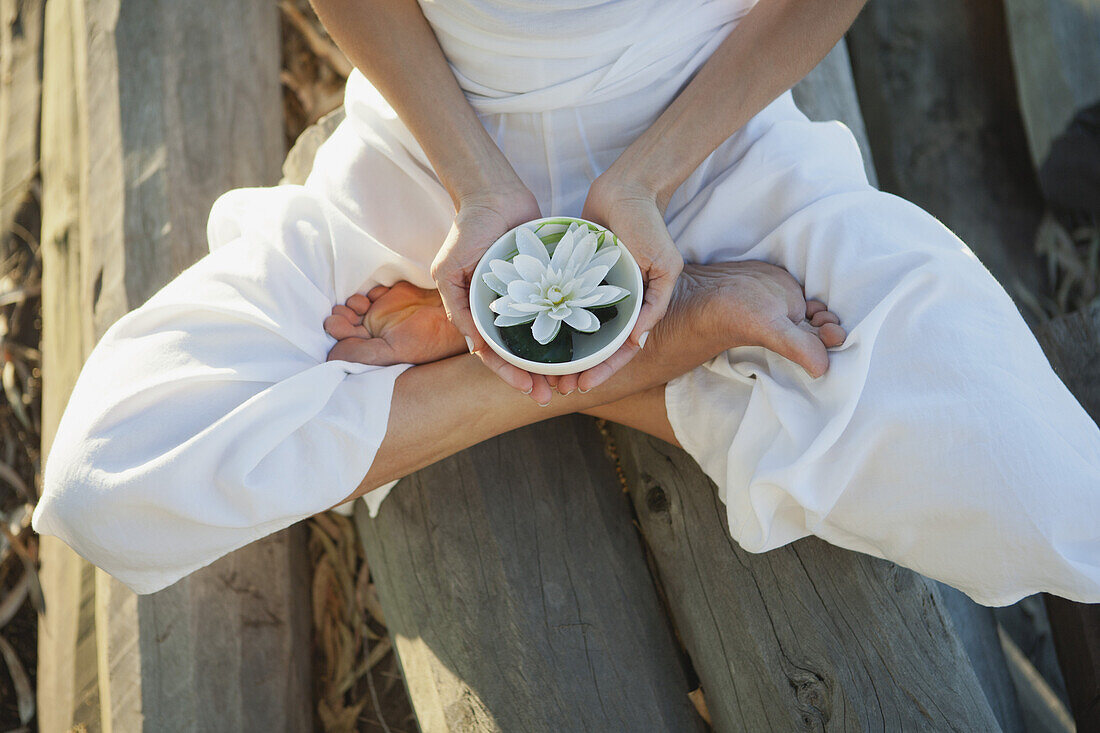 Woman sitting in lotus position, holding water lily in bowl