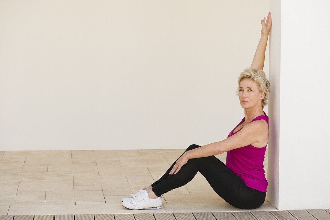 Mature woman sitting against wall, stretching arm