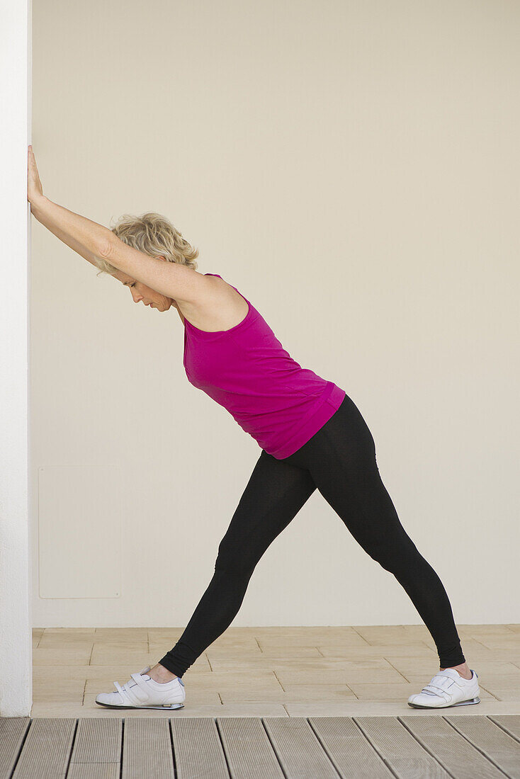 Mature woman pushing against wall, side view