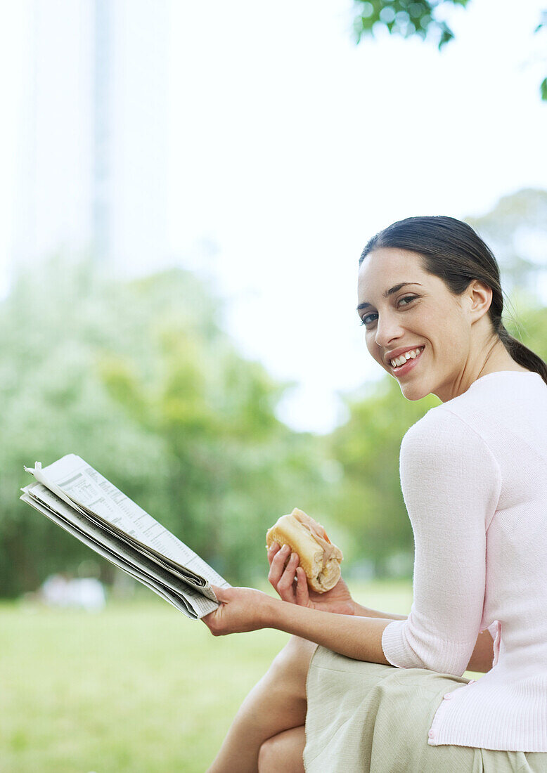 Junge Frau liest Zeitung und isst ein Sandwich im Stadtpark