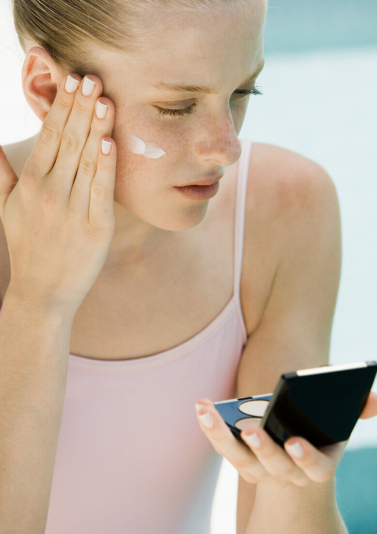 Woman applying sunscreen, looking into compact mirror