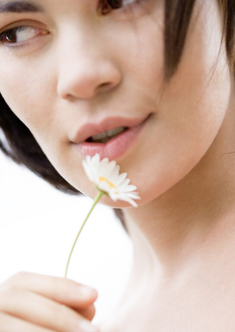 Woman holding flower next to face, close-up