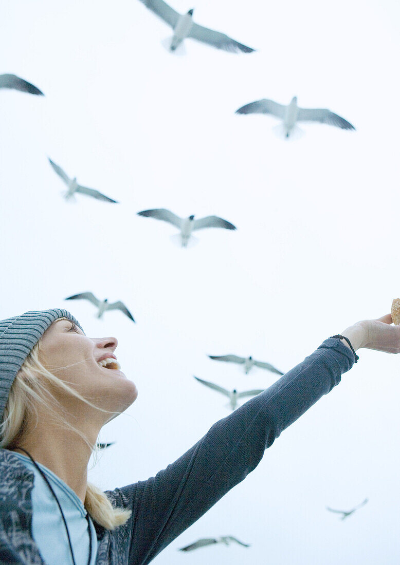 Young woman feeding seagulls in sky